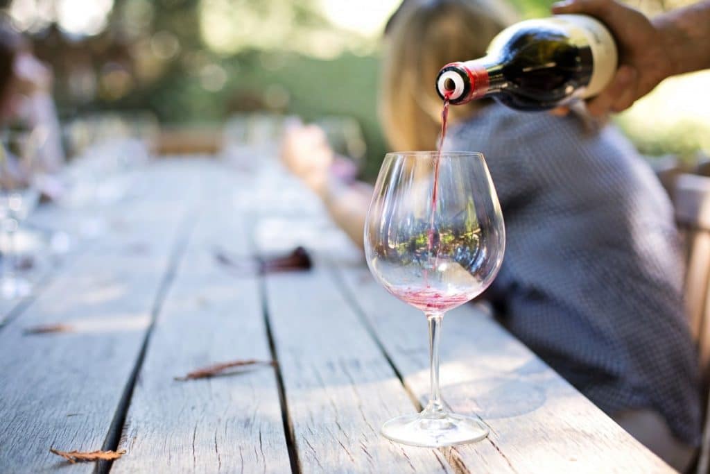 A wine bottle is being poured into a glass on a wooden table outdoors.